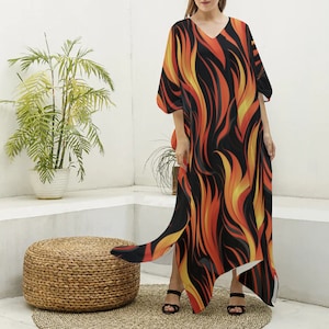 May include: A long, black, orange and yellow flowing dress with a flame pattern. The dress has a V-neck and a loose fit. The model is wearing the dress with sandals.