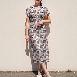 May include: A white midi dress with a wrap-style bodice and short sleeves. The dress is patterned with colorful illustrations of books. The dress has a V-neckline and a fitted silhouette, suitable for casual or semi-formal occasions.