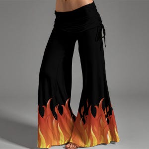 May include: Black flared pants with a high waist and a drawstring detail. The bottom of the pants features a flame design in shades of yellow, orange, and red. The pants are made of a soft, flowing fabric.