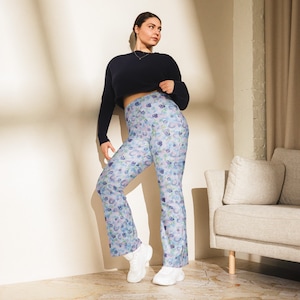 Puede incluir: Una mujer con un top negro corto y pantalones acampanados azules con estampado floral. Los pantalones tienen cintura alta y pierna ancha.