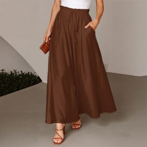 Könnte beinhalten: Braune Hose mit weitem Bein, Kordelzug in der Taille und Taschen. Die Hose wird mit braunen Riemchensandalen kombiniert. Eine kleine braune Clutch wird in der linken Hand gehalten. Geeignet für lässige oder halbformelle Anlässe.