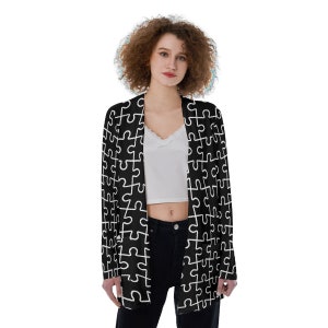 Könnte beinhalten: Ein schwarzer Cardigan mit einem weißen Puzzle-Muster. Der Cardigan ist vorne offen und hat lange Ärmel.