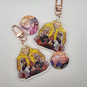May include: A collection of anime-style keychains and buttons. The keychains feature a yellow jacket design with a group of characters. The buttons display character portraits. All items have a rose gold clasp.