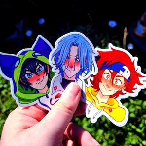 May include: Three anime-style stickers featuring male characters with distinctive hairstyles and outfits. One sticker shows a character in a green and blue cat-eared hoodie. Another has blue hair and a white jacket. The third has red hair and a yellow hoodie.