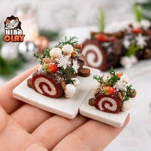 May include: Two miniature yule log cakes on white square plates. Each cake features a dark brown chocolate exterior, a red and white swirled interior, and is decorated with small white mushrooms, green moss, red berries, and white snowflakes.