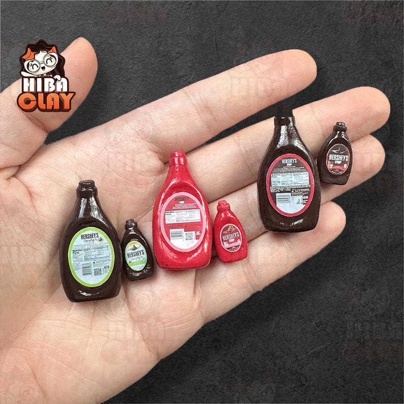May include: Miniature Hershey's syrup and ketchup bottles in various sizes. The bottles are brown and red, with labels. The image shows a collection of small, detailed food replicas, perfect for dollhouses or crafts.