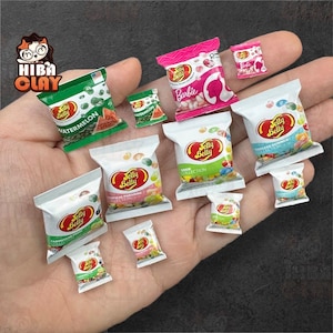 May include: Miniature Jelly Belly candy bags in various flavors, including watermelon and Barbie, are displayed. The bags are white with colorful graphics and the Jelly Belly logo. The image showcases a collection of small, detailed food replicas.