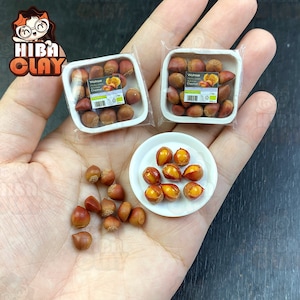 Könnte beinhalten: Ein weißer Teller mit einem Haufen gerösteter Kastanien. Im Hintergrund befinden sich zwei durchsichtige Plastikbehälter mit Etiketten, auf denen "Waitrose", "Marron Glacé" und "Chestnut" steht. Die Kastanien sind auf dem Teller und in den Behältern in einem Haufen angeordnet.