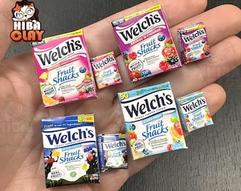 Può includere: Scatole in miniatura di Welch's Fruit Snacks in vari gusti, tra cui frutta mista e frutti di bosco e ciliegie. Le scatole sono dai colori vivaci con illustrazioni di frutta e il logo Welch's. L'immagine mostra una mano che tiene le scatole in miniatura.