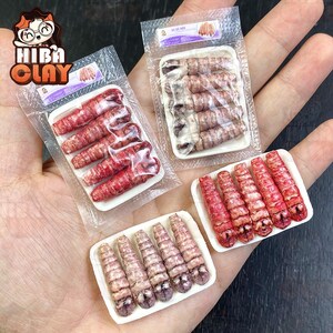 Könnte beinhalten: Drei Packungen mit Miniatur-Plastikgarnelen, jede mit einer anderen Farbe und einem anderen Muster. Die Garnelen sind in Reihen auf einem weißen Hintergrund angeordnet. Die Packungen sind mit dem Text "HiBa Clay" beschriftet.