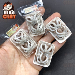 May include: Four small white plastic containers with clear plastic lids, each containing a miniature octopus made of polymer clay. The octopus is a light brown color with white tentacles. The containers are labeled with the text "Bạch Tuộc Sữa" in black.