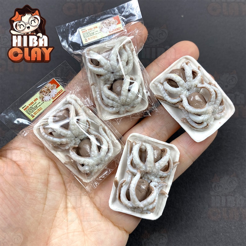 May include: Four small white plastic containers with clear plastic lids, each containing a miniature octopus made of polymer clay. The octopus is a light brown color with white tentacles. The containers are labeled with the text "Bạch Tuộc Sữa" in black.