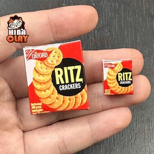 May include: Miniature boxes of Ritz Crackers, featuring the brand name in bold white letters on a black circle, with a stack of crackers on the front. The boxes are red and white, with the Oxford logo. One box is larger than the other.