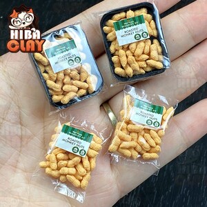 May include: Four miniature packages of roasted monkey nuts, each with a green and white label that reads "Market St. Roasted Monkey Nuts". The packages are in various forms, including a clear plastic bag and a clear plastic container.
