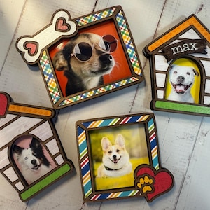 Puede incluir: Una colección de marcos de fotos de madera con temática de perros. Un marco tiene forma de hueso con un corazón, otro es una caseta para perros con el nombre "max", y los otros son rectangulares con bordes coloridos. Cada marco contiene una foto de un perro.