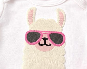 May include: A white baby bodysuit featuring an embroidered graphic of a cream-colored llama wearing bright pink sunglasses with dark gray lenses. The llama has pink inner ears and a small black nose and mouth, centered on the chest of the garment.