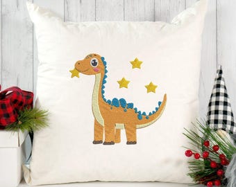 May include: A square white throw pillow featuring an embroidered design of a tan dinosaur with blue spikes along its back. The dinosaur is surrounded by three yellow embroidered stars. The pillow has a smooth, solid white fabric finish.