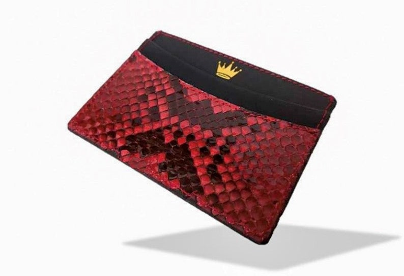 May include: A red snakeskin card holder with a black leather interior and a gold crown logo.