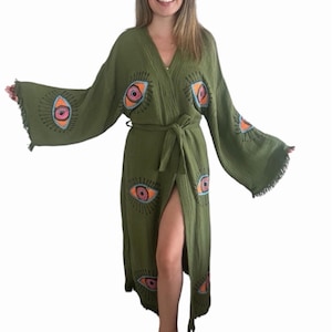 May include: A long, green robe with a wrap closure and a side slit. The robe has a fringe trim and is decorated with embroidered eyes in shades of pink, orange, and blue.