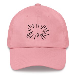 Peut inclure: Une casquette de baseball rose avec un motif brodé noir en forme d'étoile éclatante avec un diamant au centre.
