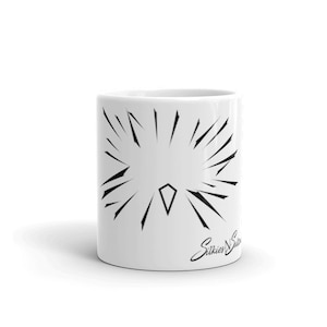 May include: White ceramic mug with a black geometric design of a starburst with a diamond in the center. The mug has the text "Stikies N Stitches" in black cursive writing on the bottom right side.