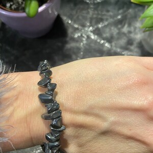 May include: A black hematite stone bracelet with irregular shaped stones. The bracelet is on a person's wrist.