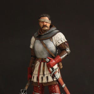 May include: A detailed figurine of a medieval warrior wearing a metal breastplate, chainmail collar, and red leather gloves. The figure has a blindfold over the eyes, carries a spiked mace in one hand, and has a sword in a red scabbard at the hip.