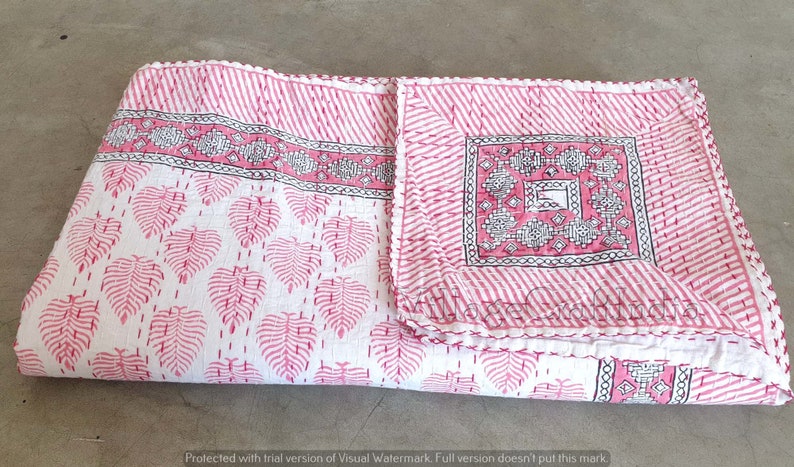 May include: A pink and white kantha quilt with a leaf pattern and a geometric design in the center. The quilt is folded in half and has a white fringe around the edges.