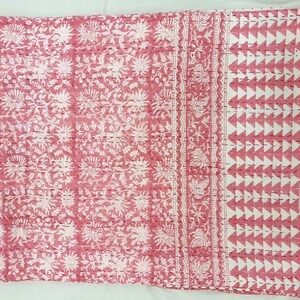 K&ouml;nnte beinhalten: Eine rosa und wei&szlig; gemusterte Steppdecke. Die Steppdecke hat auf der linken Seite ein sich wiederholendes Blumendesign, in der Mitte einen dekorativen Rand und auf der rechten Seite ein geometrisches Dreieckmuster. Die Steppdecke besteht aus einem weichen, gesteppten Stoff.