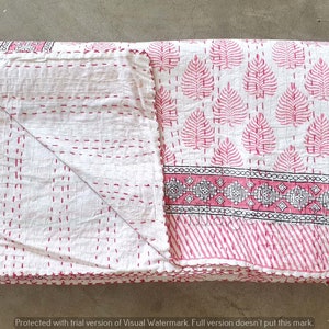 May include: A pink and white kantha quilt with a leaf pattern and a border of geometric designs. The quilt is folded in half and has a fringe edge.