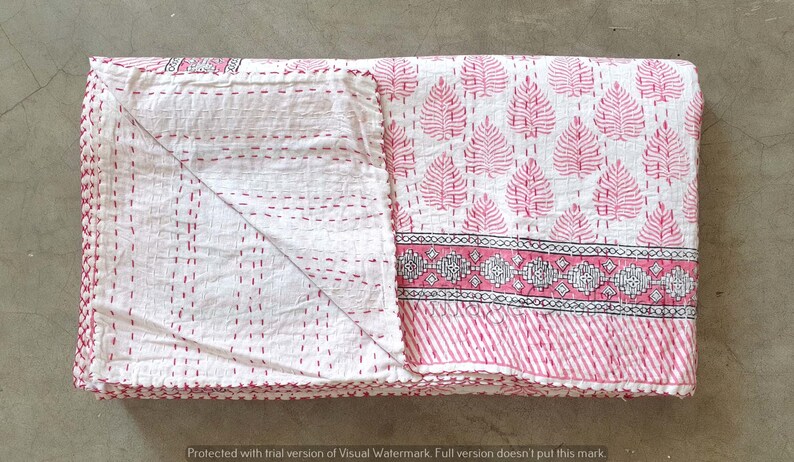 May include: A pink and white kantha quilt with a leaf pattern and a border of geometric designs. The quilt is folded in half and has a fringe edge.