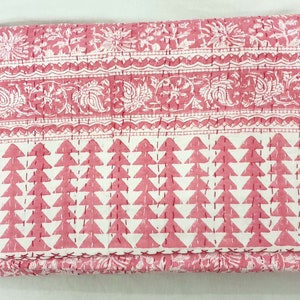 Puede incluir: Un edredón rosa y blanco doblado con un patrón geométrico y floral. El edredón presenta un diseño de triángulo repetido en la sección inferior y patrones florales y de cachemira en la sección superior. El edredón está cosido a mano.