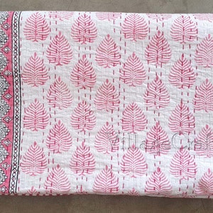 May include: A white cotton kantha quilt with a pink leaf pattern and a pink and white border. The quilt is hand-stitched and has a traditional Indian design.