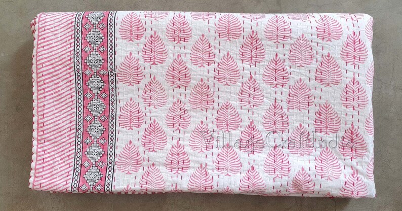May include: A white cotton kantha quilt with a pink leaf pattern and a pink and white border. The quilt is hand-stitched and has a traditional Indian design.