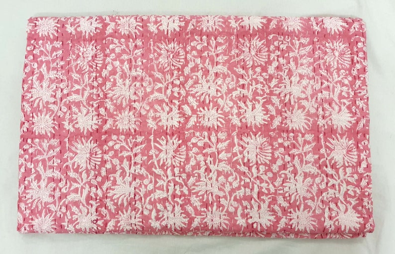 K&ouml;nnte beinhalten: Eine rosa und wei&szlig; gemusterte Steppdecke. Die Steppdecke weist ein sich wiederholendes Design aus gro&szlig;en Blumen und Bl&auml;ttern auf, die mit einem kontrastierenden Faden zusammengen&auml;ht sind. Die Gesamt&auml;sthetik ist weich und feminin, geeignet f&uuml;r Bettw&auml;sche oder dekorative Zwecke.