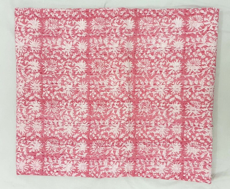 K&ouml;nnte beinhalten: Ein Textil mit rosa und wei&szlig;em Blumenmuster. Das Design zeigt sich wiederholende wei&szlig;e Blumen- und Blattmotive auf rosa Hintergrund. Der Stoff scheint mit sichtbaren N&auml;hten im gesamten Design gesteppt zu sein.