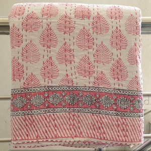 May include: White cotton kantha quilt with a pink leaf pattern and a pink and black border. The quilt is folded and hanging on a rack.