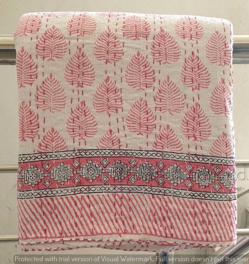 May include: White cotton kantha quilt with a pink leaf pattern and a pink and black border. The quilt is folded and hanging on a rack.