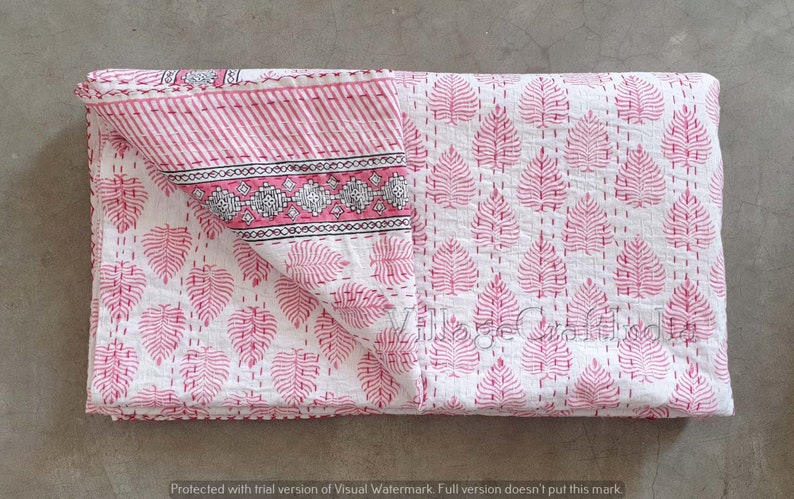 May include: A pink and white kantha quilt with a leaf pattern. The quilt is folded in half and has a decorative border.