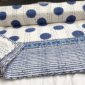 May include: White kantha quilt with a blue polka dot pattern and a blue and white striped border. The quilt is folded and rolled up.