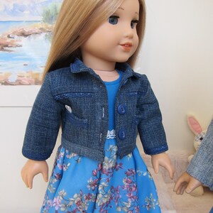 May include: A doll wearing a blue denim jacket over a blue floral dress. The doll has long blonde hair and blue eyes.