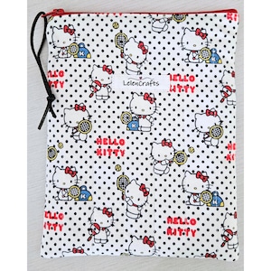 Puede incluir: Bolsa blanca con cremallera roja y cordón negro. La bolsa está cubierta con un patrón de lunares negros y personajes de dibujos animados de Hello Kitty jugando al tenis. Las palabras "Hello Kitty" están impresas en rojo.