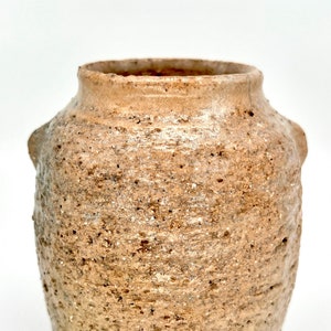 May include: A small, brown, ceramic vase with a rough, textured surface. The vase has a rounded body and a wide opening.