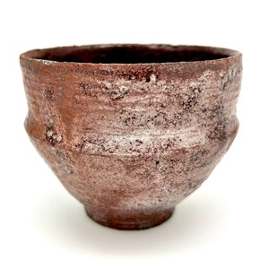 May include: A small, rustic, brown ceramic bowl with a white glaze. The bowl has a rounded shape and a slightly flared rim.