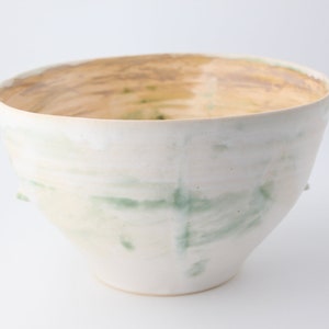May include: A white ceramic bowl with green and brown glaze. The bowl has a wide rim and a rounded bottom.