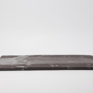 Puede incluir: Una bandeja rectangular de color gris oscuro con un patrón de salpicaduras blancas.
