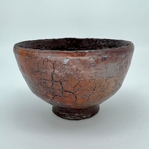 May include: A brown ceramic bowl with a crackled glaze. The bowl has a wide, round opening and a slightly flared rim. The bowl is sitting on a white surface.