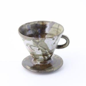 Peut inclure: Ensemble verseuse à café et soucoupe en céramique. La verseuse conique est dotée d'une petite anse, et l'ensemble comprend une soucoupe ronde assortie. La verseuse et la soucoupe sont émaillées dans des tons de gris, de brun et de blanc.