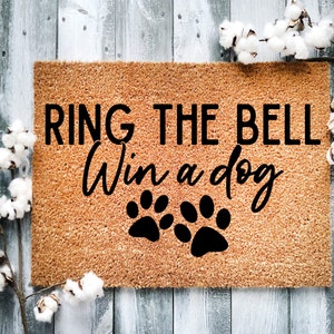 May include: A brown coir doormat with the text "RING THE BELL Win a dog" in black lettering and two black paw prints.