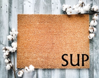May include: A brown coir doormat with the word "SUP" in black lettering.